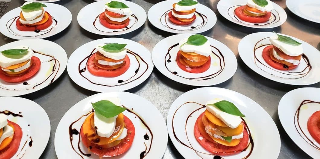 Artfully arranged plates of layered tomatoes, peaches, and mozzarella topped with basil and balsamic drizzle.