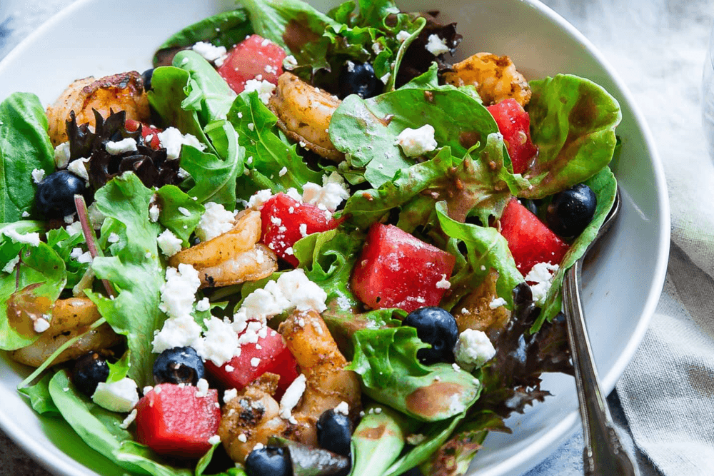 A fresh salad with shrimp, watermelon, blueberries, and feta cheese on a bed of mixed greens.