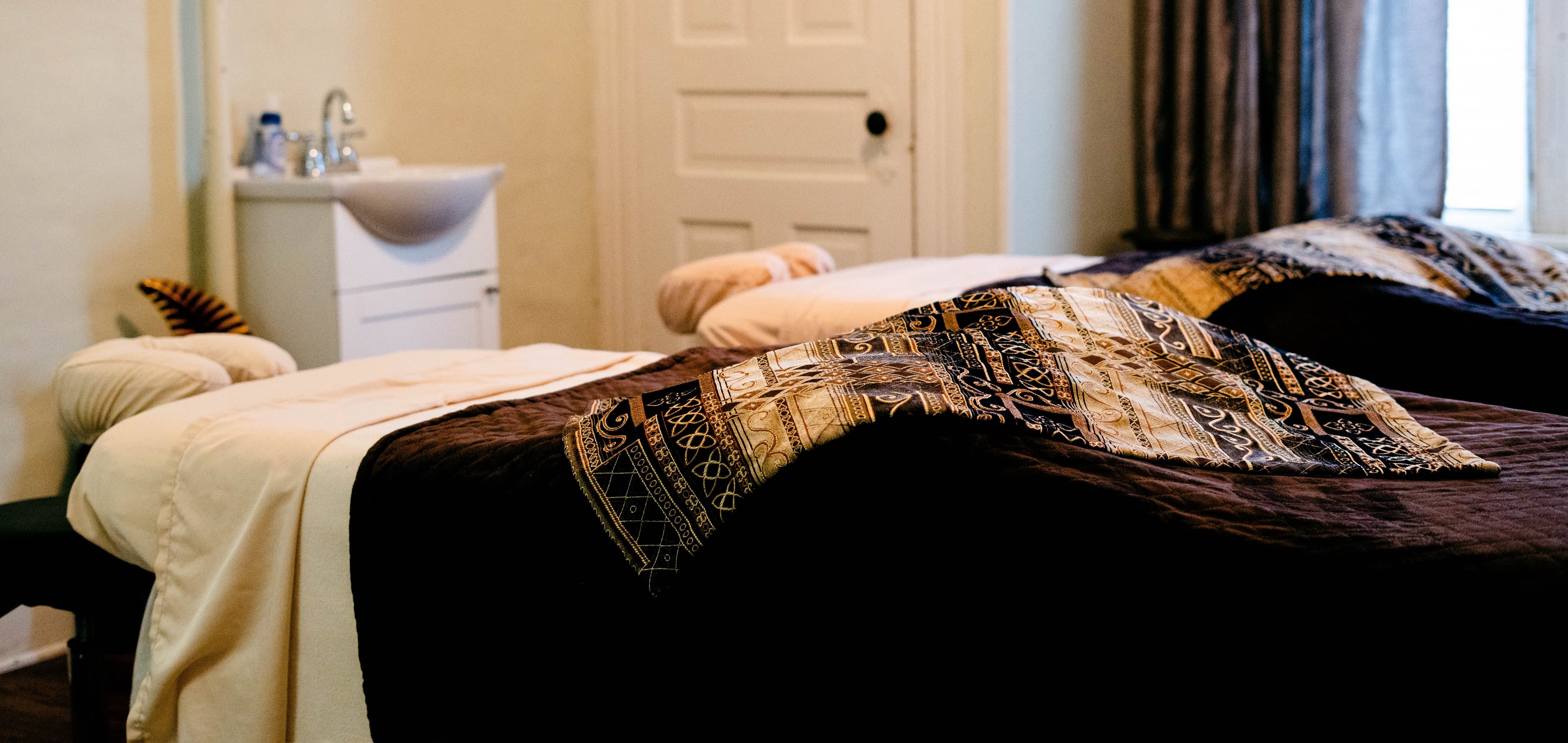 A calm massage therapy room with two treatment tables covered in patterned blankets.