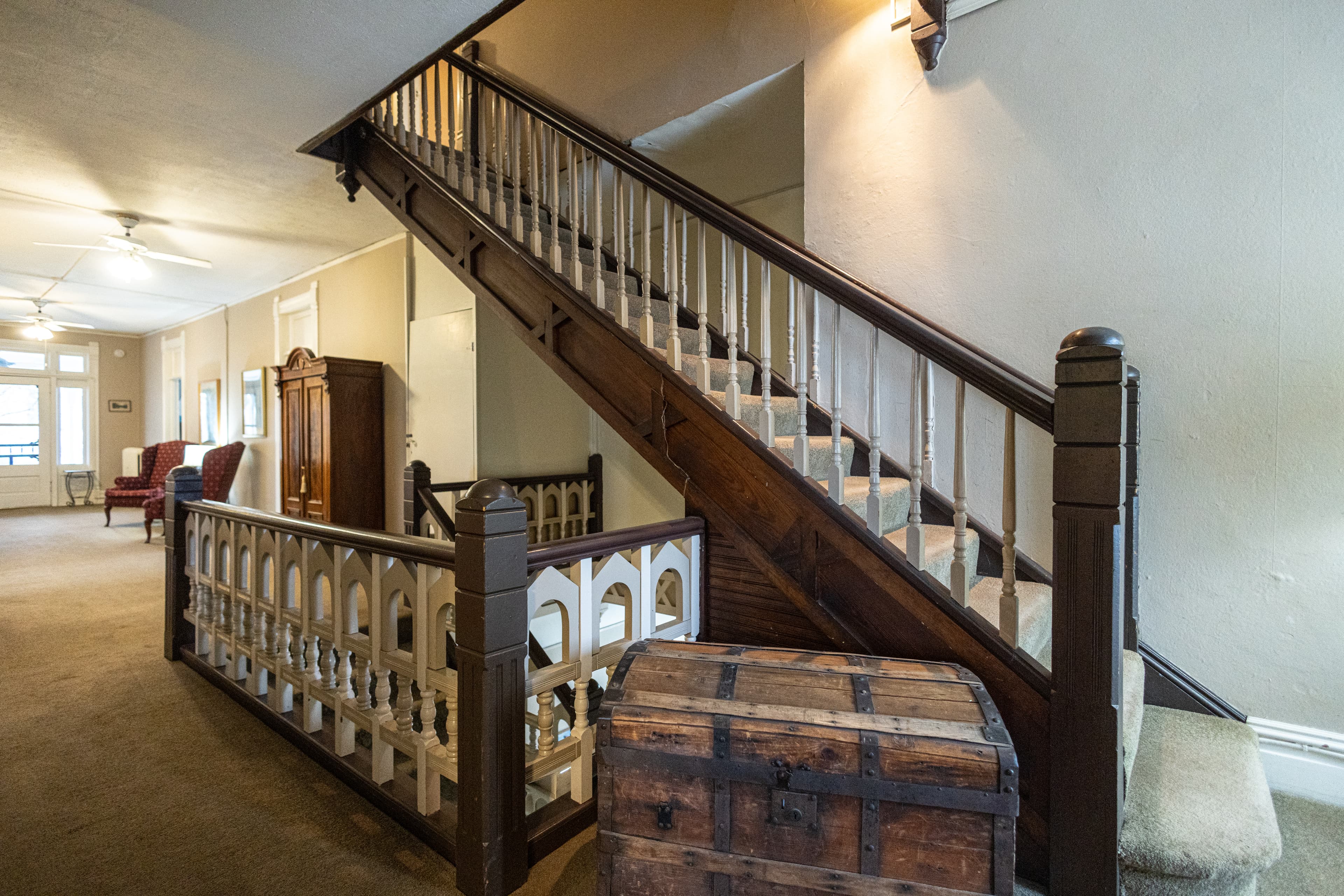 A cozy hallway featuring a wooden staircase, vintage furniture, and a chest.