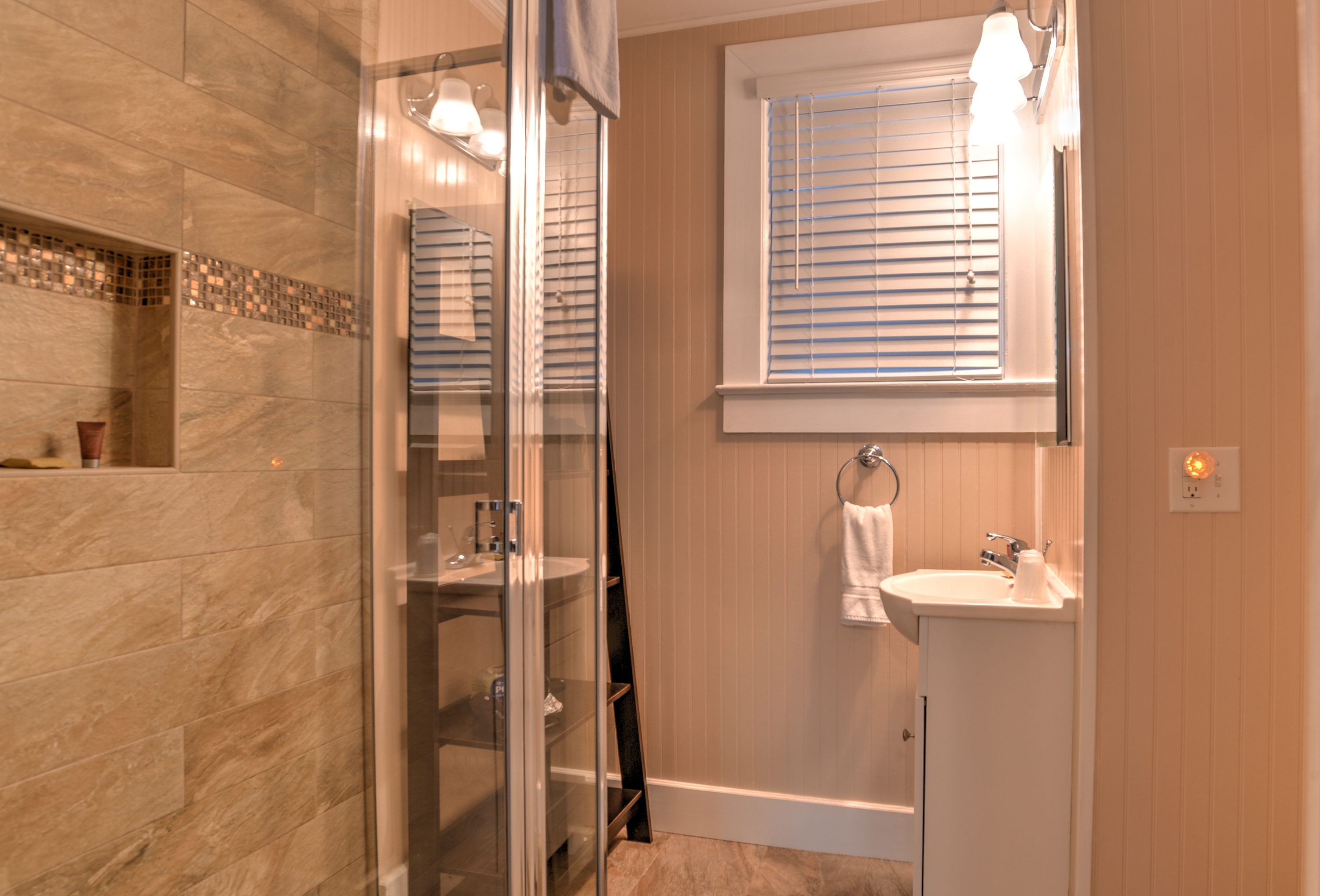 Bathroom features a large walk-in shower, white stand alone sink, and tall shelving unit.