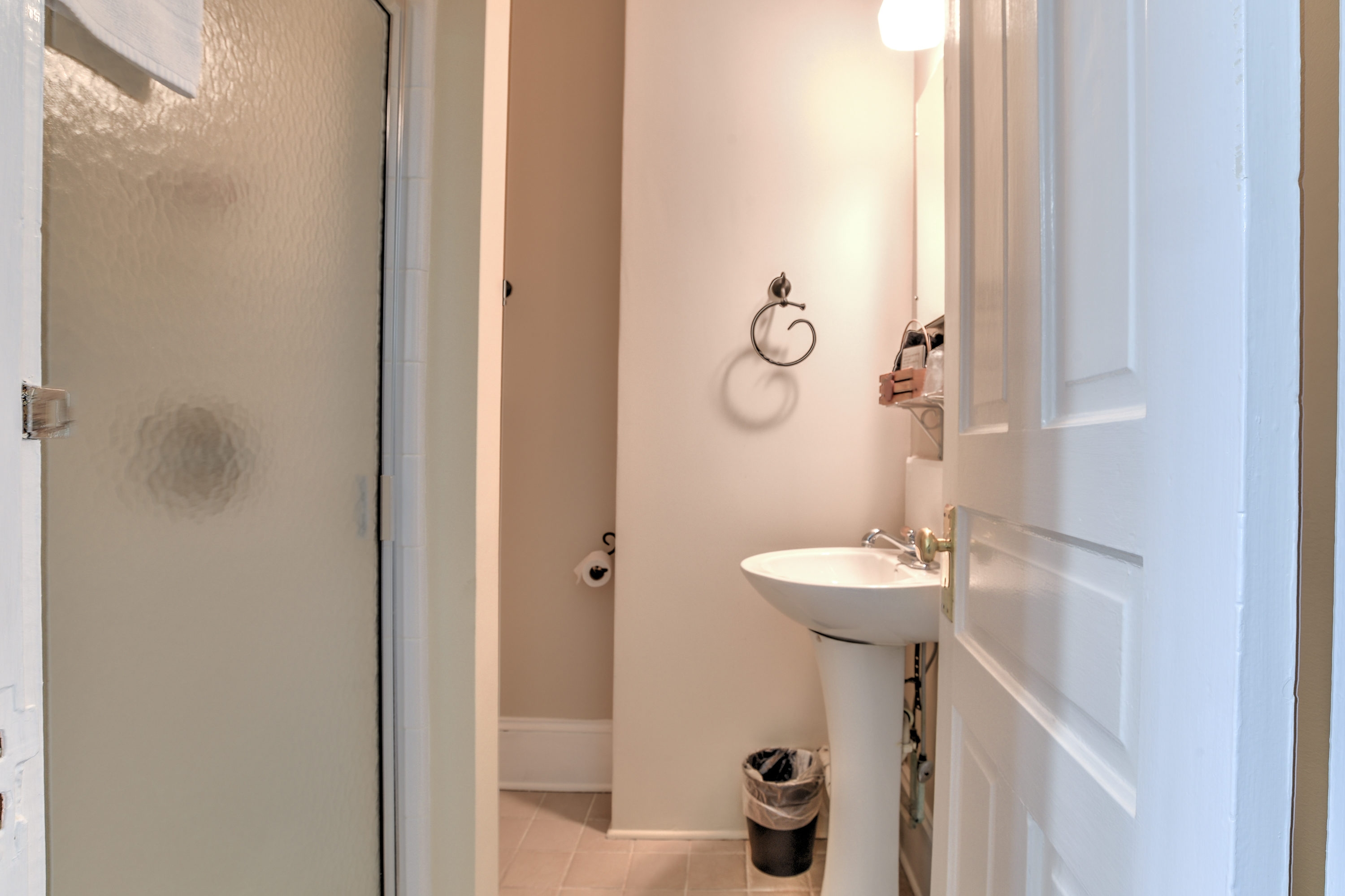 Bathroom features a small shower with glass door and white stand alone sink.