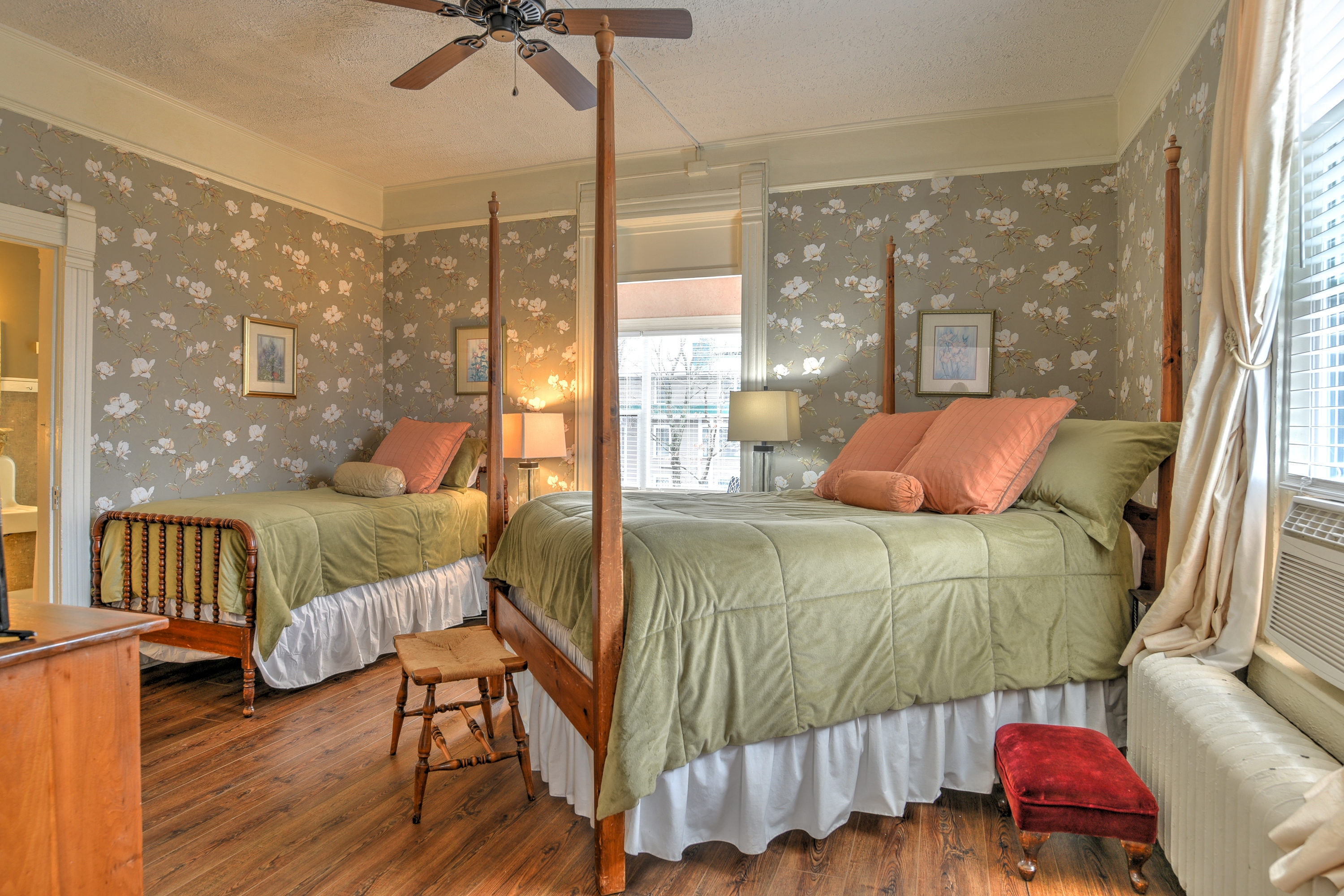 Room features wood flooring, floral wallpaper, four posted queen bed, and twin bed.