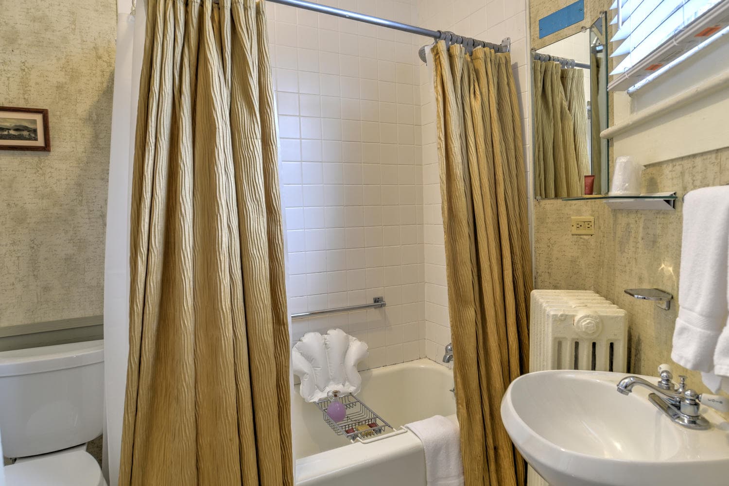 Bathroom features a bathtub with wrap-around shower curtain, white stand alone sink, and white toilet.