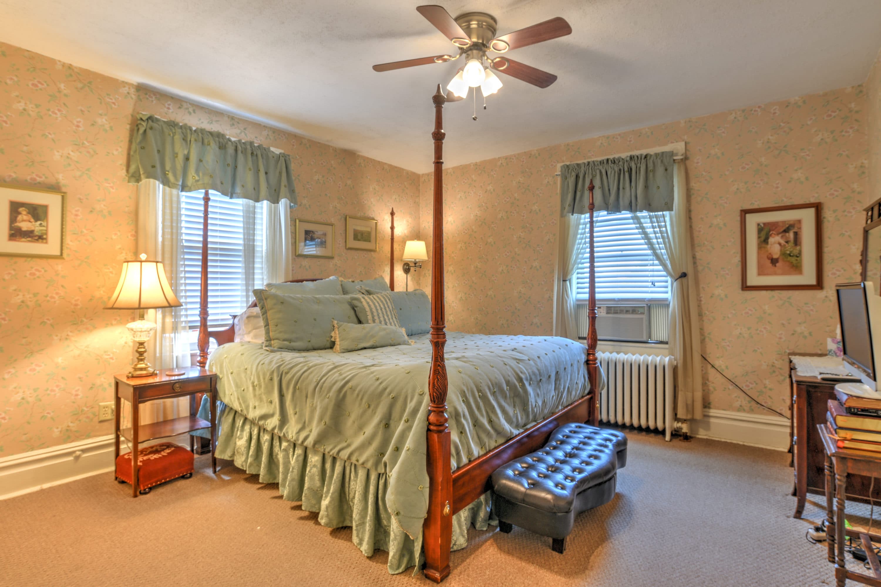 Room features four posted king bed with wooden night stand and desk.
