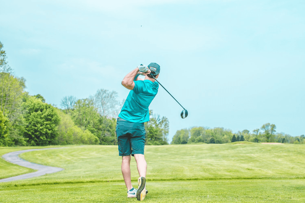 A golfer swings a driver on a sunny day at a green course.