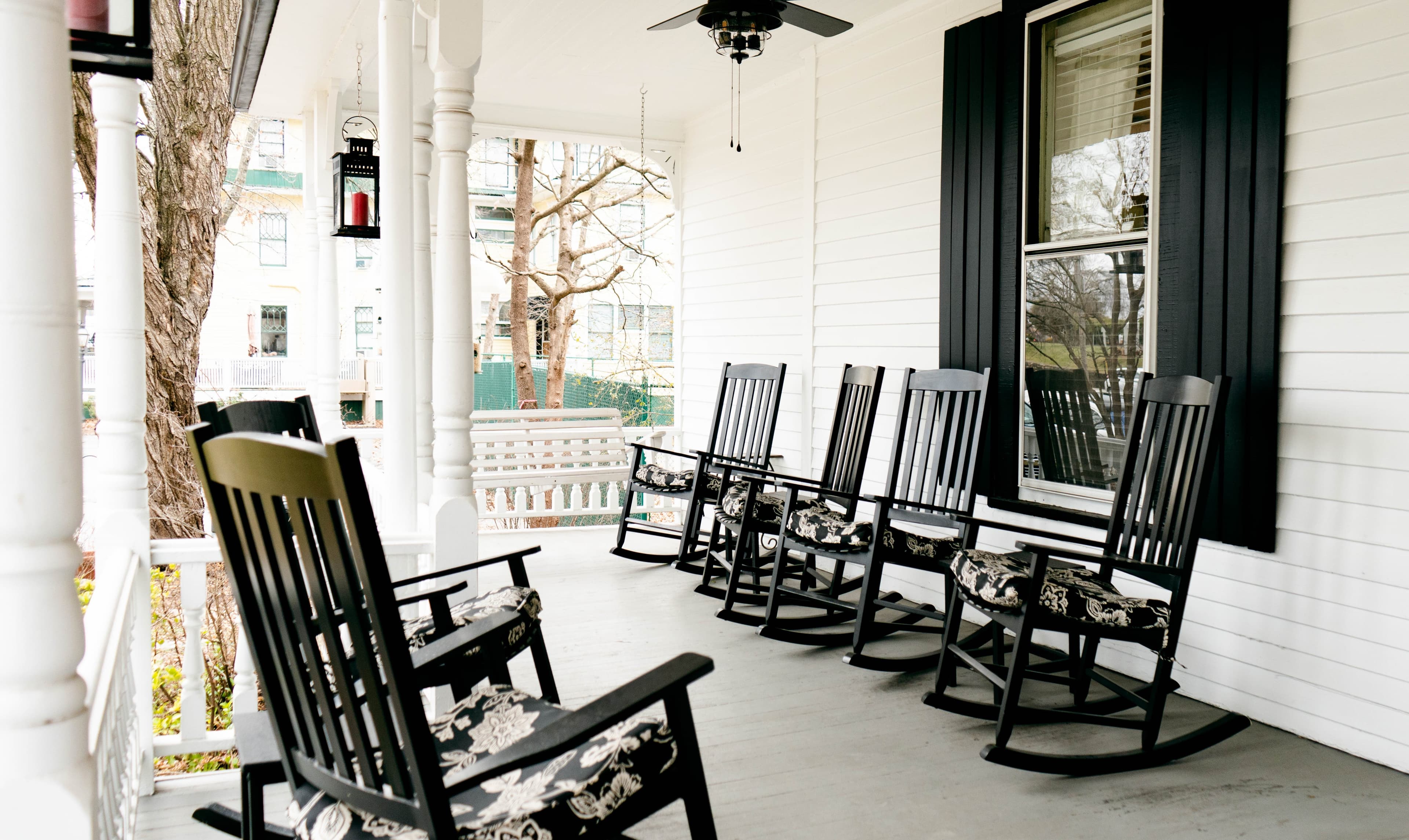 A porch featuring several black rocking chairs with floral cushions.