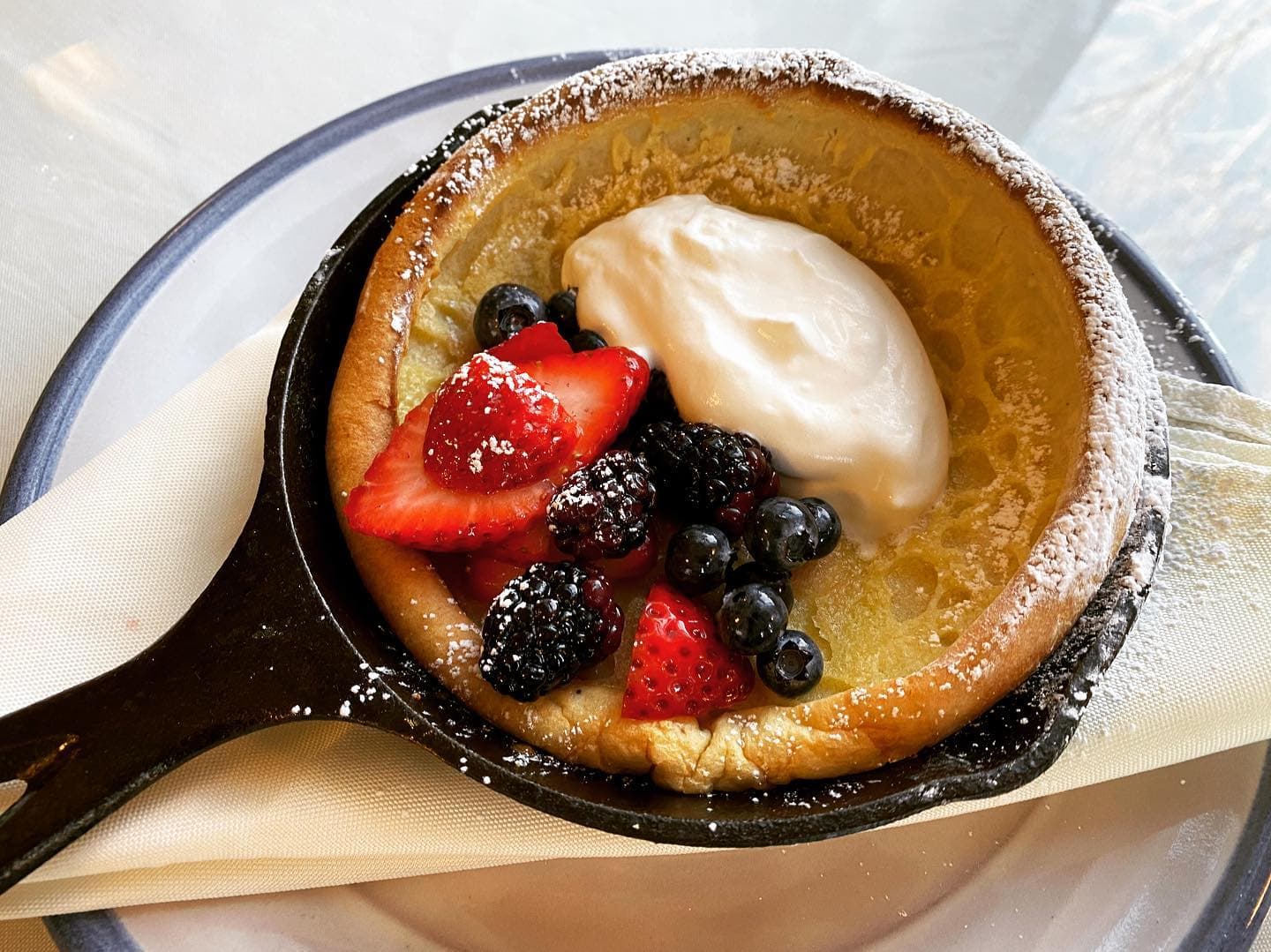 A Dutch baby pancake topped with fresh berries and whipped cream, served in a skillet.