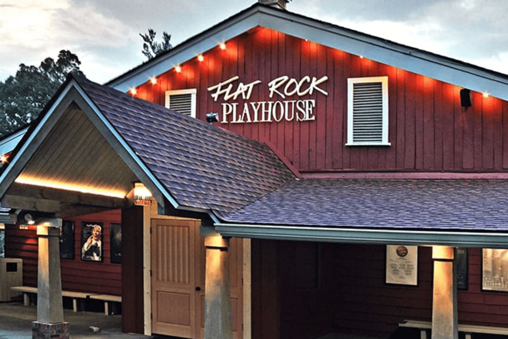 Exterior view of the Flat Rock Playhouse, featuring a red wooden facade and illuminated signage.