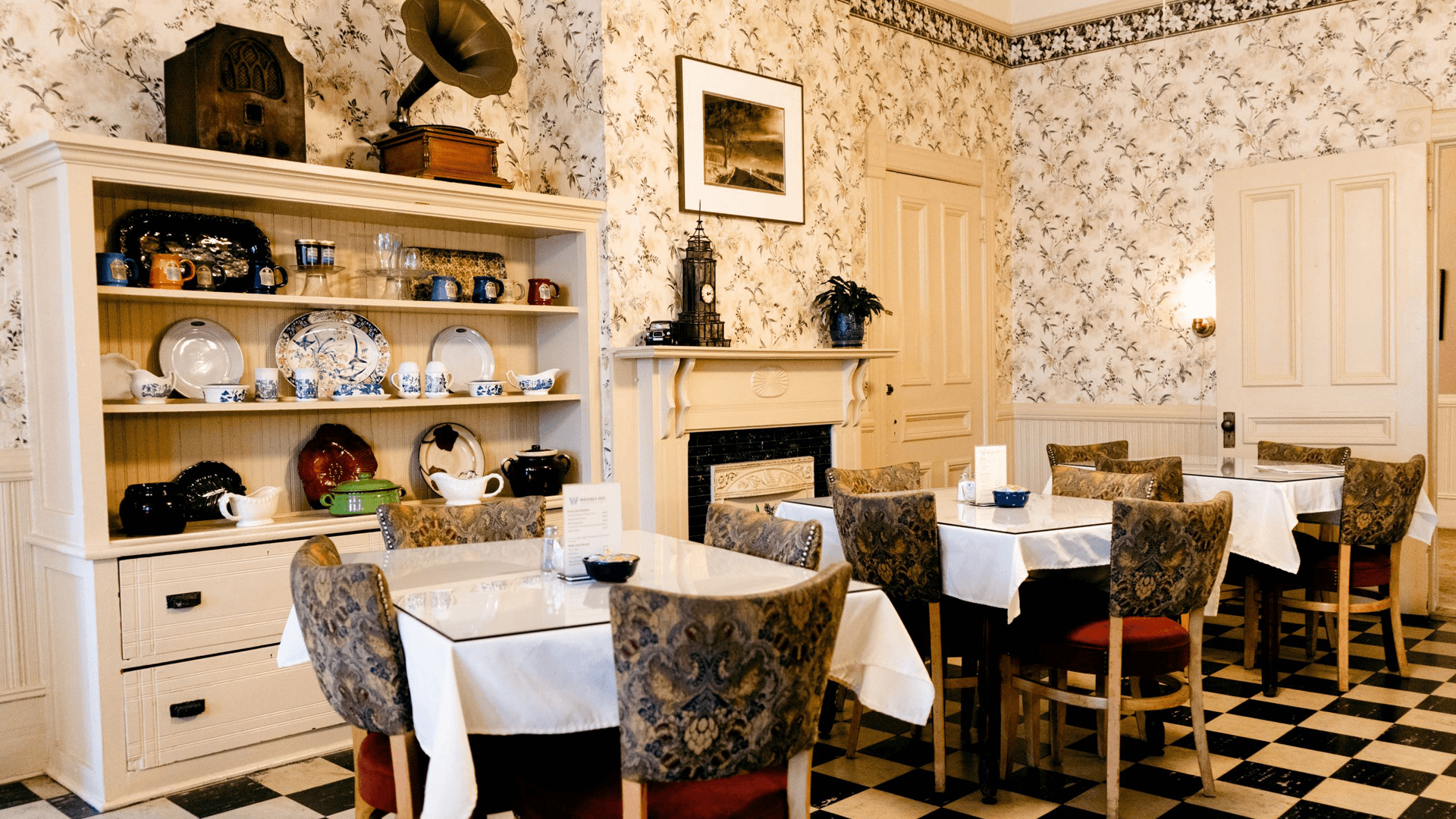 A cozy dining area featuring vintage decor, patterned chairs, and a display of dishware.