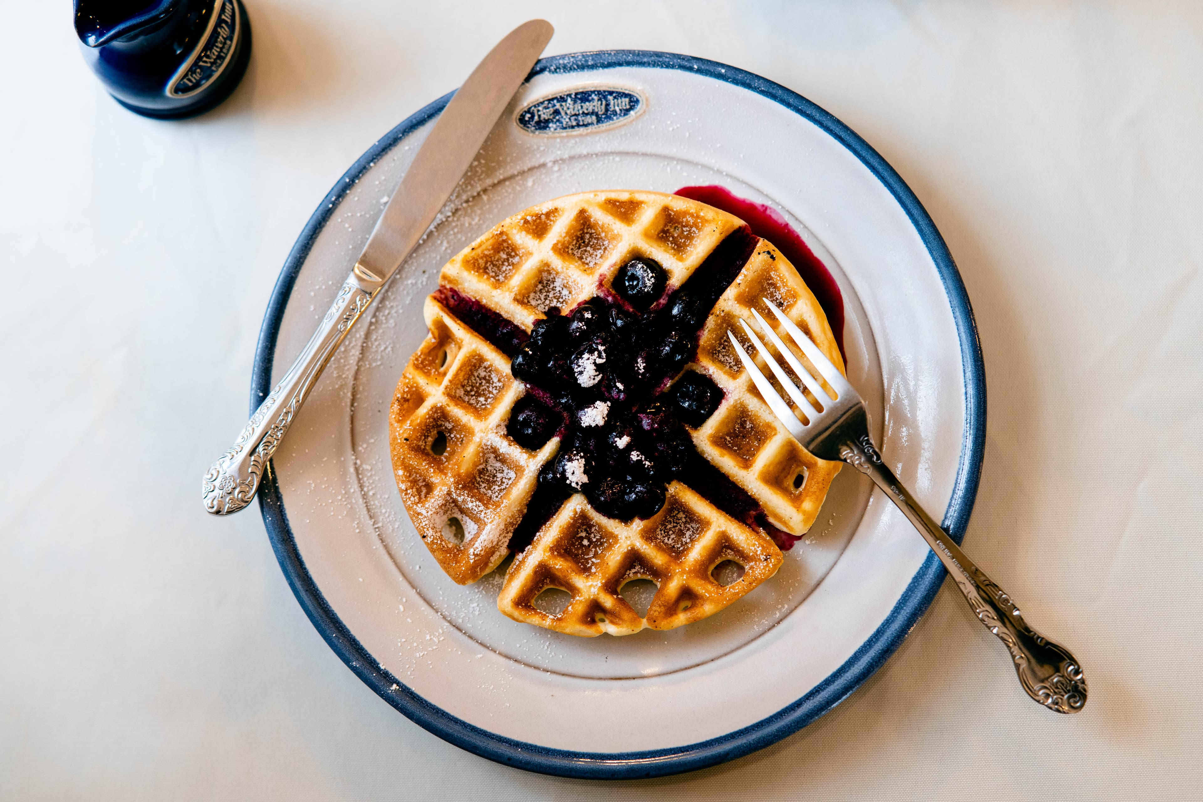 A plate of waffles topped with blueberries and powdered sugar, accompanied by a knife and fork.