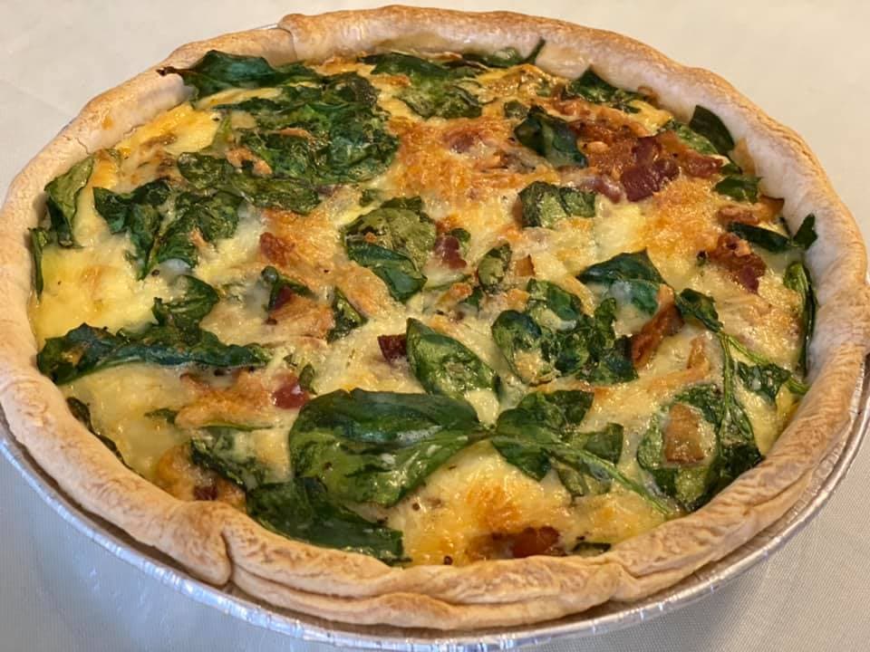 A golden-brown quiche filled with spinach and bits of bacon.